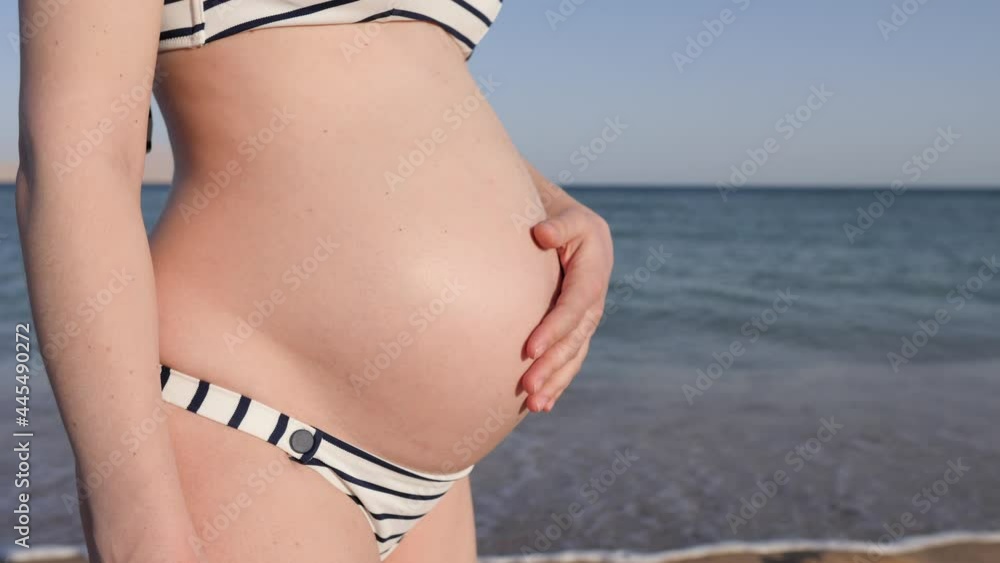 Close up of hand of pregnant woman in a swimsuit stroking her belly. Sea in the background Close up of hand of pregnant woman in a swimsuit stroking her belly. Sea in the background