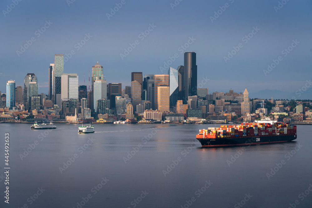 A container ship freighter sits at anchor in Elliott Bay on Puget Sound as the Seattle Skyline rises in the background.
