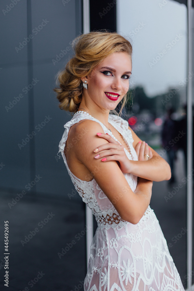 Fototapeta premium Beautiful blond bride in white wedding dress standing near mirror window outdoors.