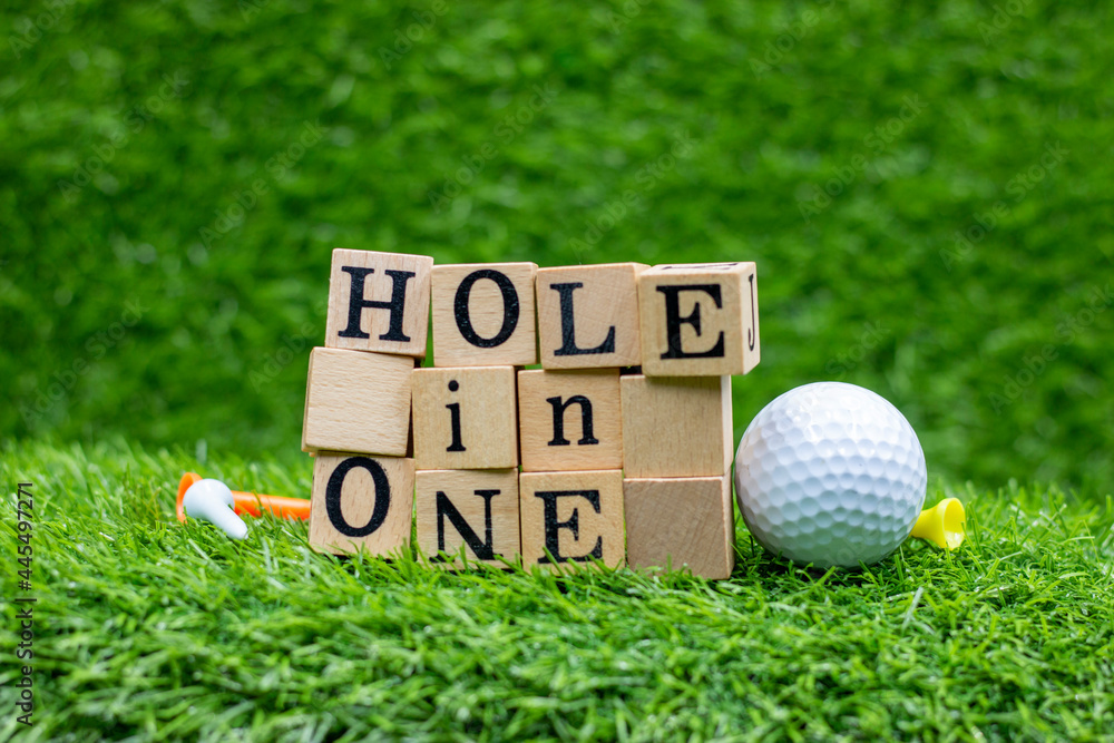 Hole in one wooden black with golf ball are on green grass with tee. n golf,