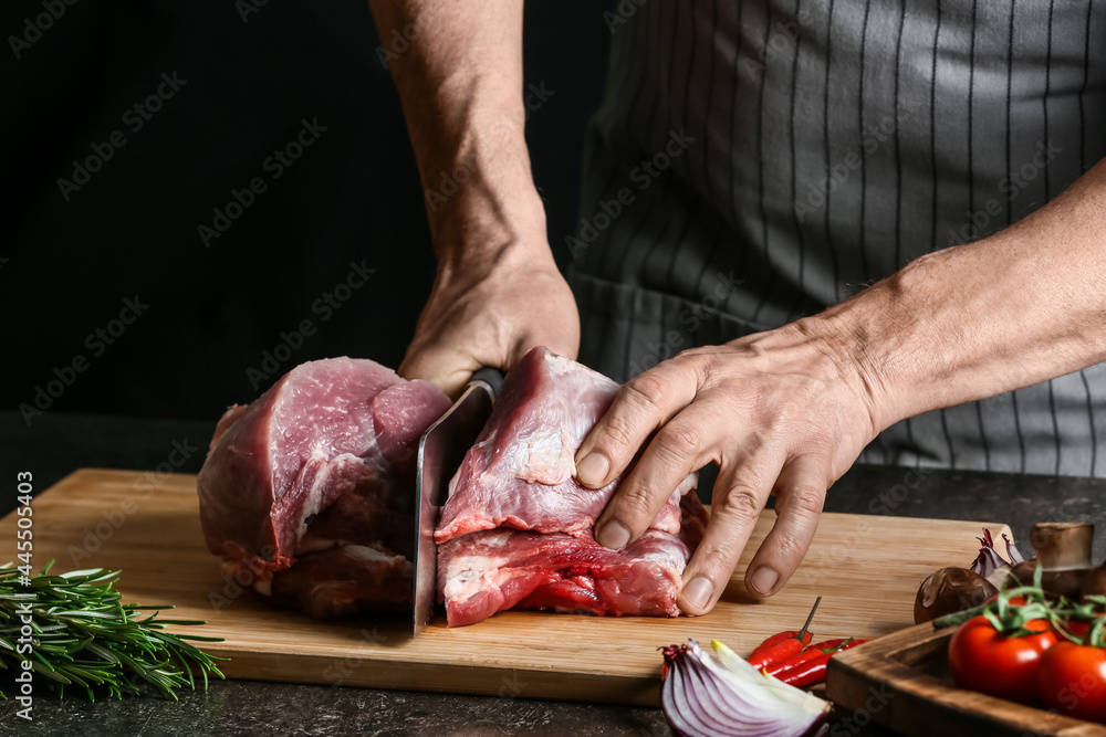 Man cutting raw pork meat on dark background