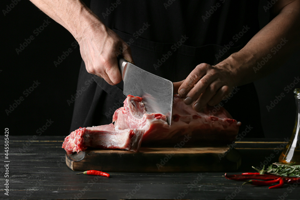 Man cutting raw pork meat on dark wooden table