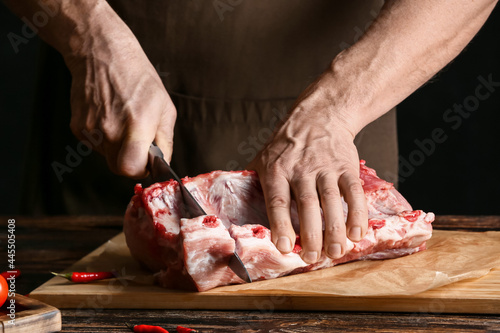 Man cutting raw pork ribs on wooden table, closeup