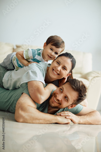 Happy family makes human pyramid while lying on floor at home and looking at camera.