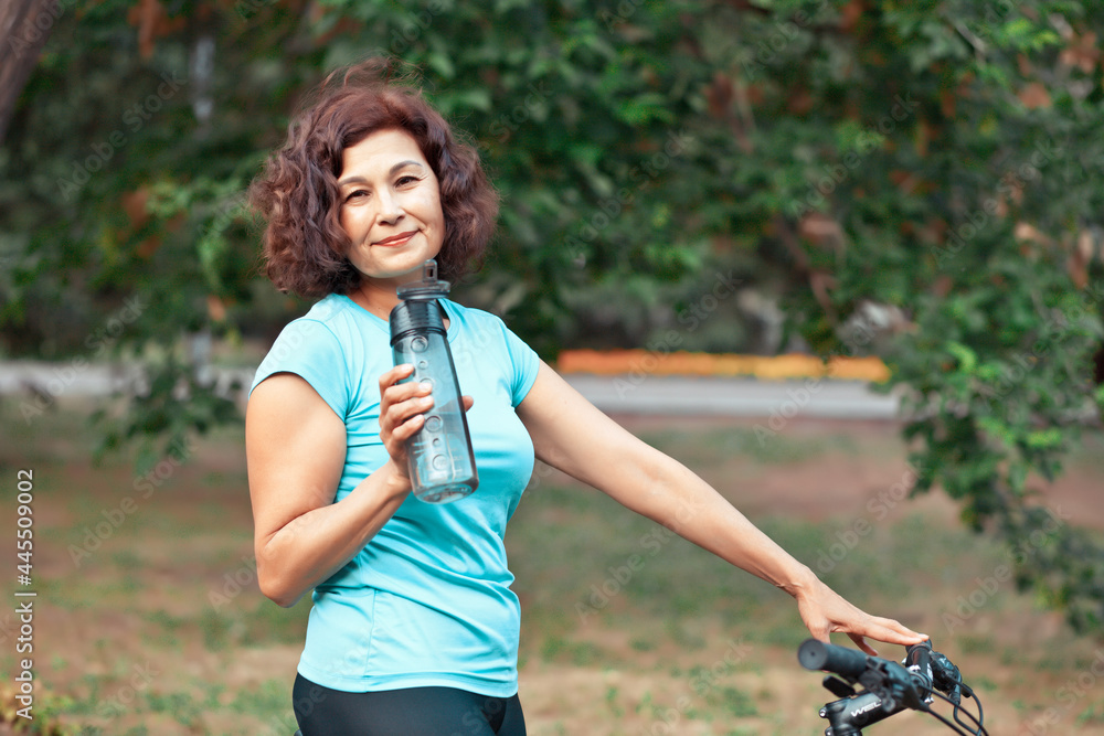 Middle age senior woman on bike cycle ride in countryside park outdoor and drink water from bottle Middle age senior woman on bike cycle ride in countryside park outdoor and drink water from bottle
