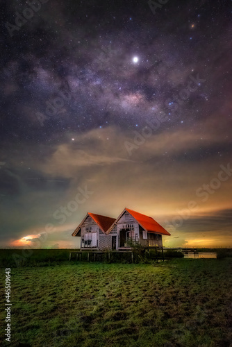 Twin-roofed old wooden house that farmers in Thailand built for shelter to escape the heat from the sun and rain while they do farming. This image taken at night with beautiful milky way in the sky.