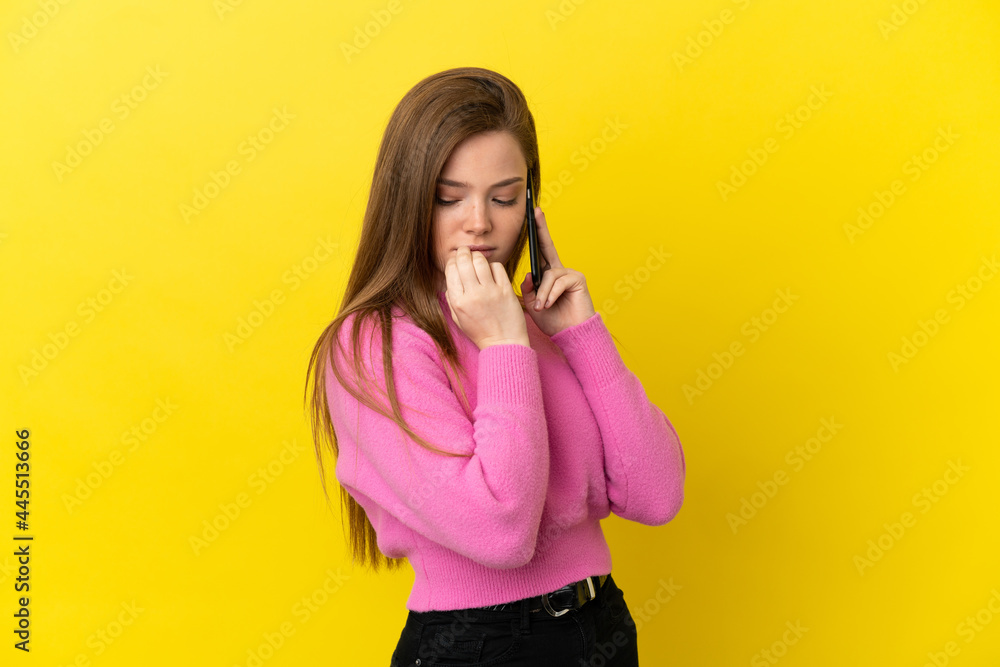 Teenager girl using mobile phone over isolated yellow background having doubts Teenager girl using mobile phone over isolated yellow background having doubts