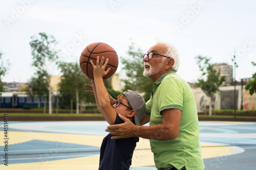 A happy little boy is playing basketball with his grandfather.