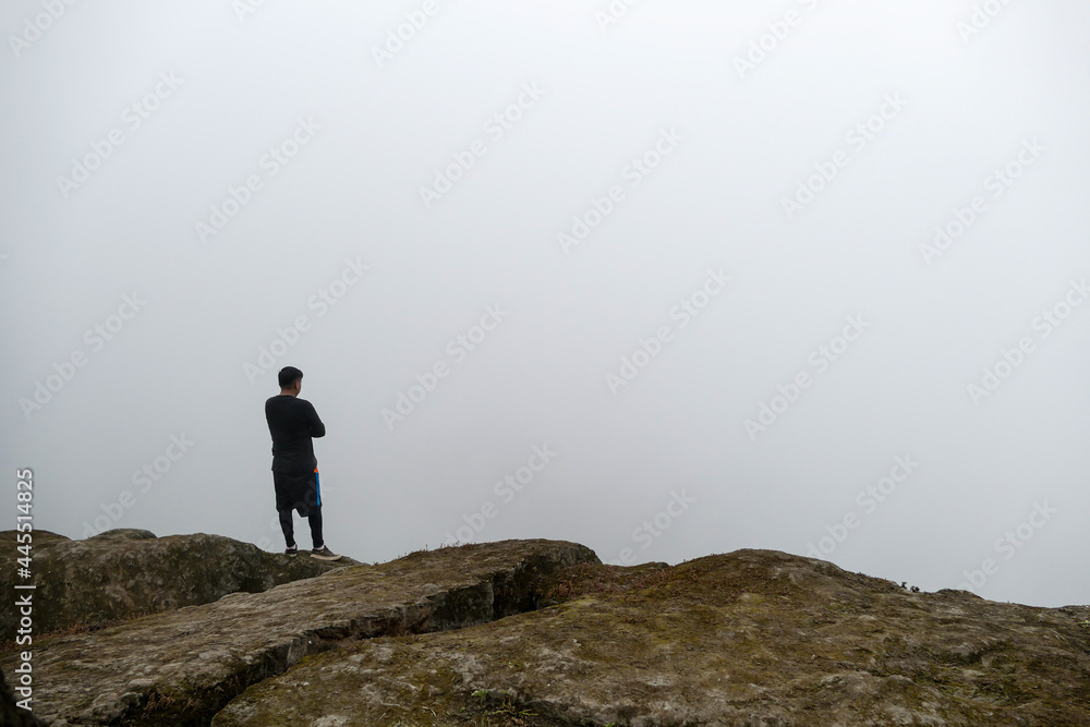 Man standing on cliff in a valley, looking at the mist.
