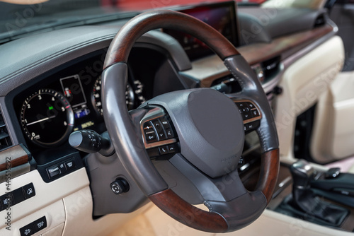 Car dashboard and steering wheel with media control buttons. Beige cockpit with exclusive wood decoration. Luxury vehicle interior