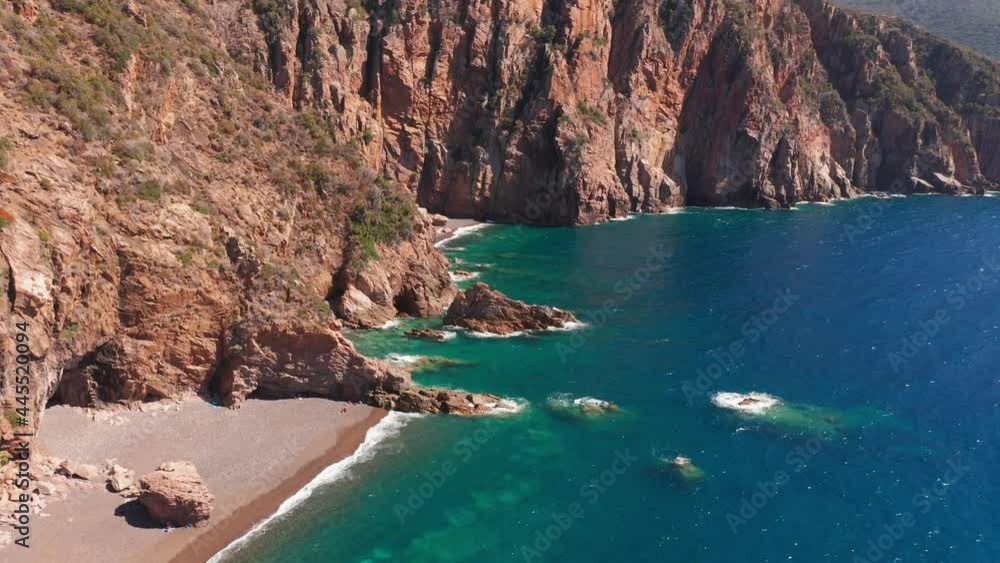 Aerial view of red rock cliffs mountain, sand beach, waves crushing on the beach. Colored sea, blue turquoise, high red cliffs on both side, green bushes of vegetation. Aerial view of red rock cliffs mountain, sand beach, waves crushing on the beach. Colored sea, blue turquoise, high red cliffs on both side, green bushes of vegetation.