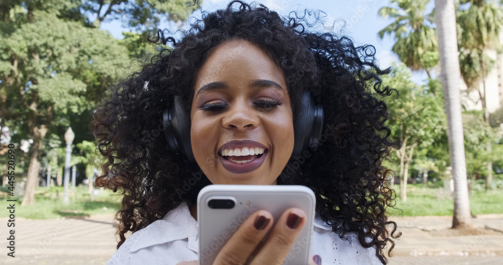 © Nexa - Young curly hair black woman walking using cell phone. Texting on street. Big city.