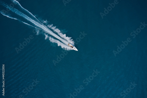 Speed boat faster movement on the water top view. Speedboat movement on the water. Large white boat driving on dark water. Speedboat on dark blue water aerial view. Speedboat wave speed water. © Berg