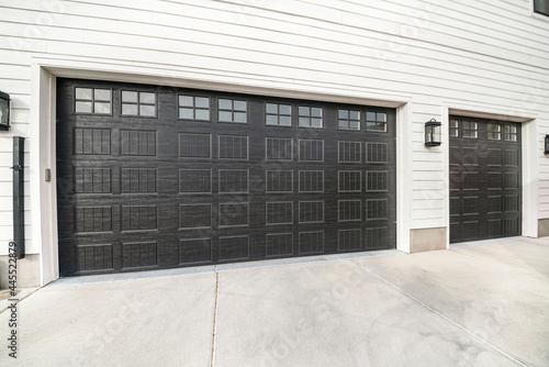 Two black garage doors with window panels and wall lighting