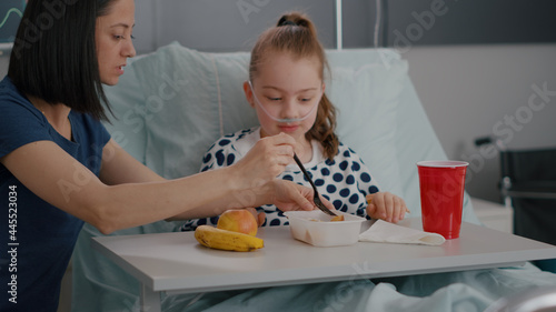 Фотография Portrait of hospitalized little chid lying in bed in recovery examination room while having food meal lunch in hospital ward