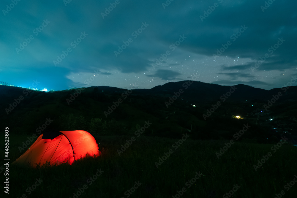 Glowing red tent with hikers sleeping in the wild mountains under ...