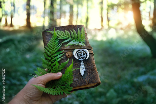 Magic witch book with amulet and fern leaves in hand on natural forest background. Esoteric Ritual, spiritual practice. Mysticism, divination, modern wicca occultism concept. atmosphere mystical image