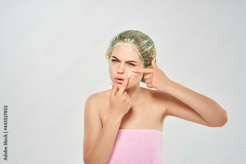 woman in a pink towel squeezes out black dots on her face light background woman in a pink towel squeezes out black dots on her face light background
