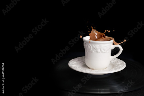 closeup of cappuccino coffee in a white cup and saucer on a black background with splashes and drops of liquid in all directions  the concept of a cafe menu  coffee time