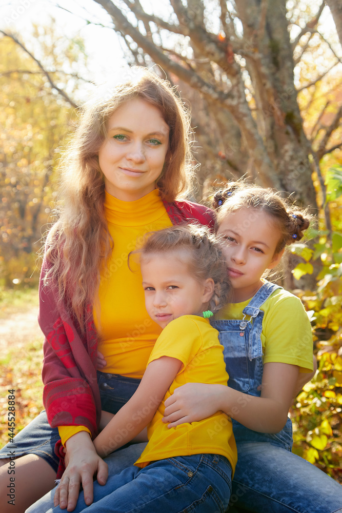 Two young little girl and his mother with blonde hair in an autumn park on a yellow and orange leaf background. Family walking in forest Two young little girl and his mother with blonde hair in an autumn park on a yellow and orange leaf background. Family walking in forest