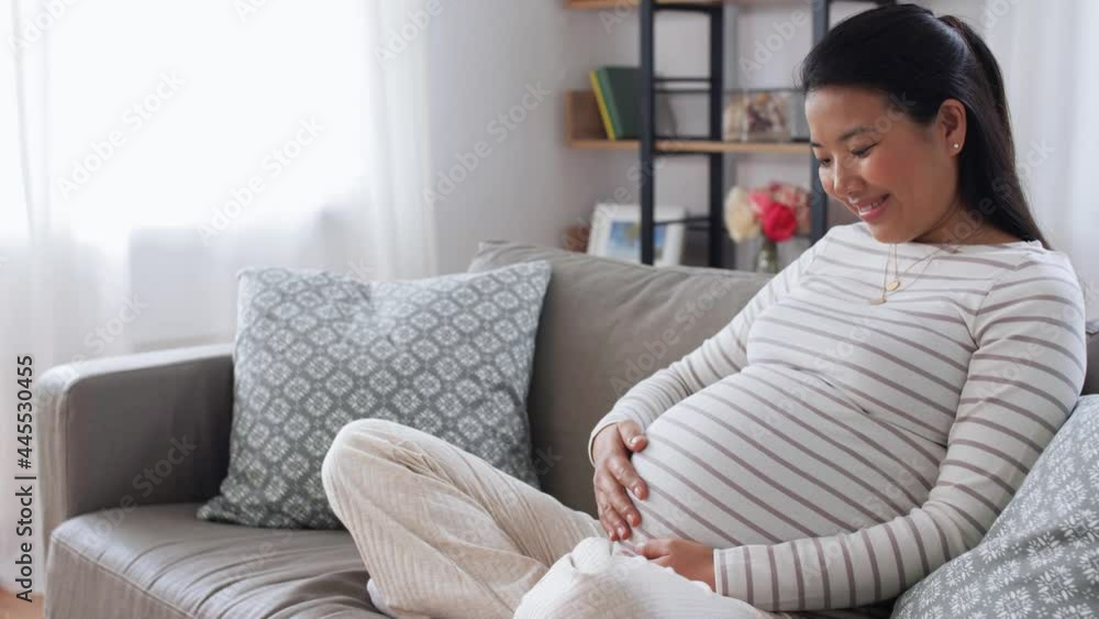 pregnancy, rest, people and expectation concept - happy smiling pregnant asian woman sitting on sofa at home pregnancy, rest, people and expectation concept - happy smiling pregnant asian woman sitting on sofa at home