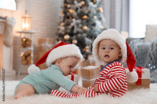 Cute children in Santa hats on floor in room with Christmas tree © New Africa