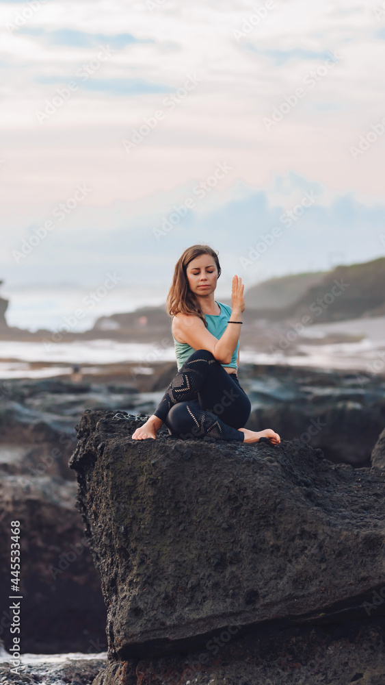 Girl doing yoga by the sea while sitting on a stone.