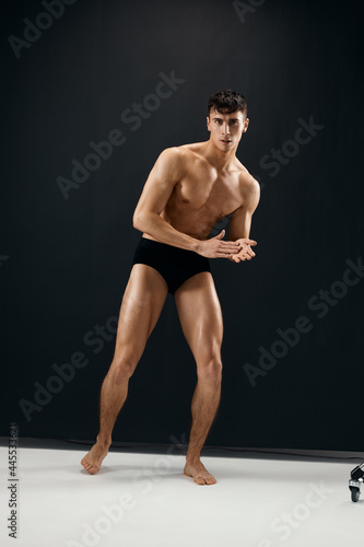 sporty man in black macho shorts posing dark background