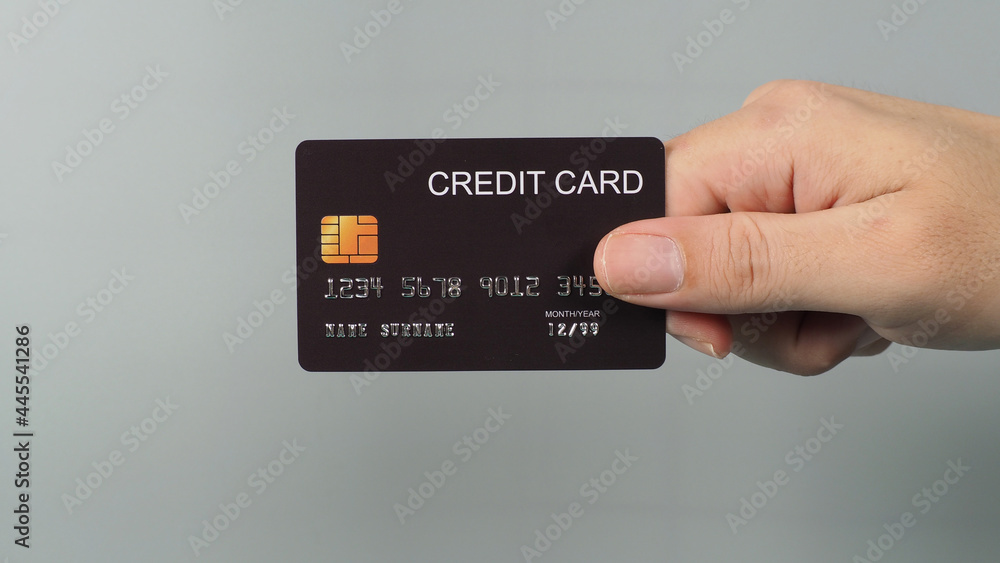 Hand is holding black credit card isolated on grey background. Hand is holding black credit card isolated on grey background.