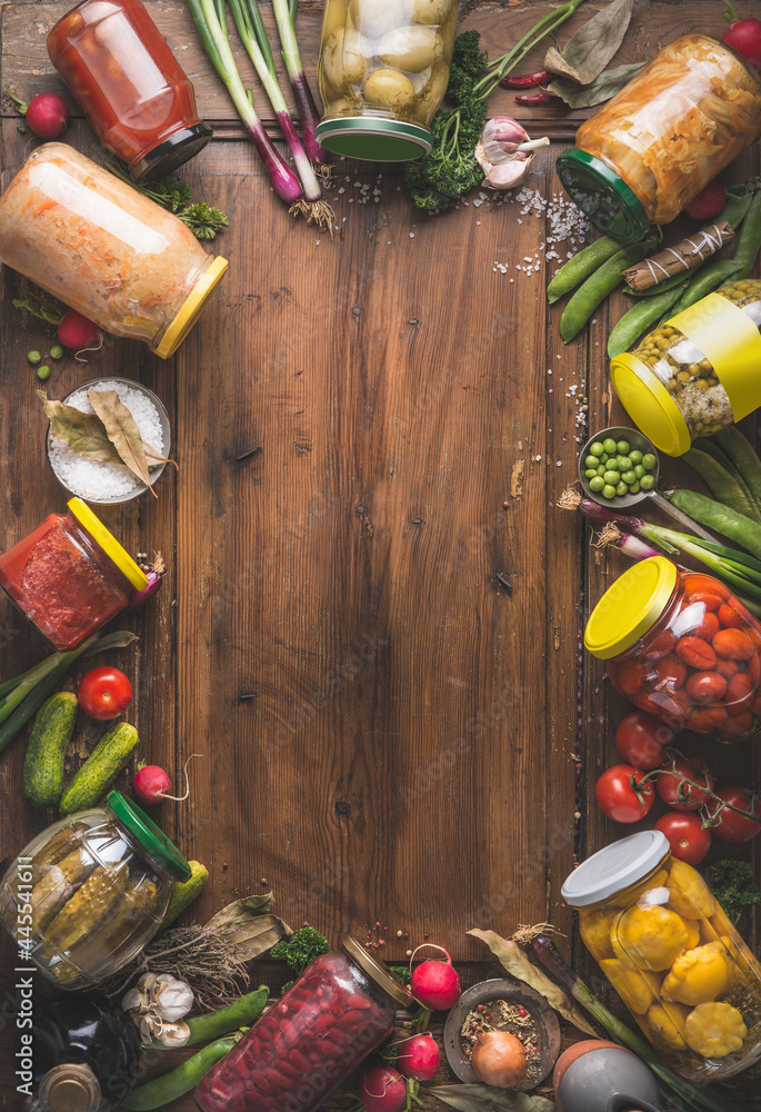 Various canned vegetables in jars on wooden background, top view. Frame. Seasonal homemade harvest preserving.