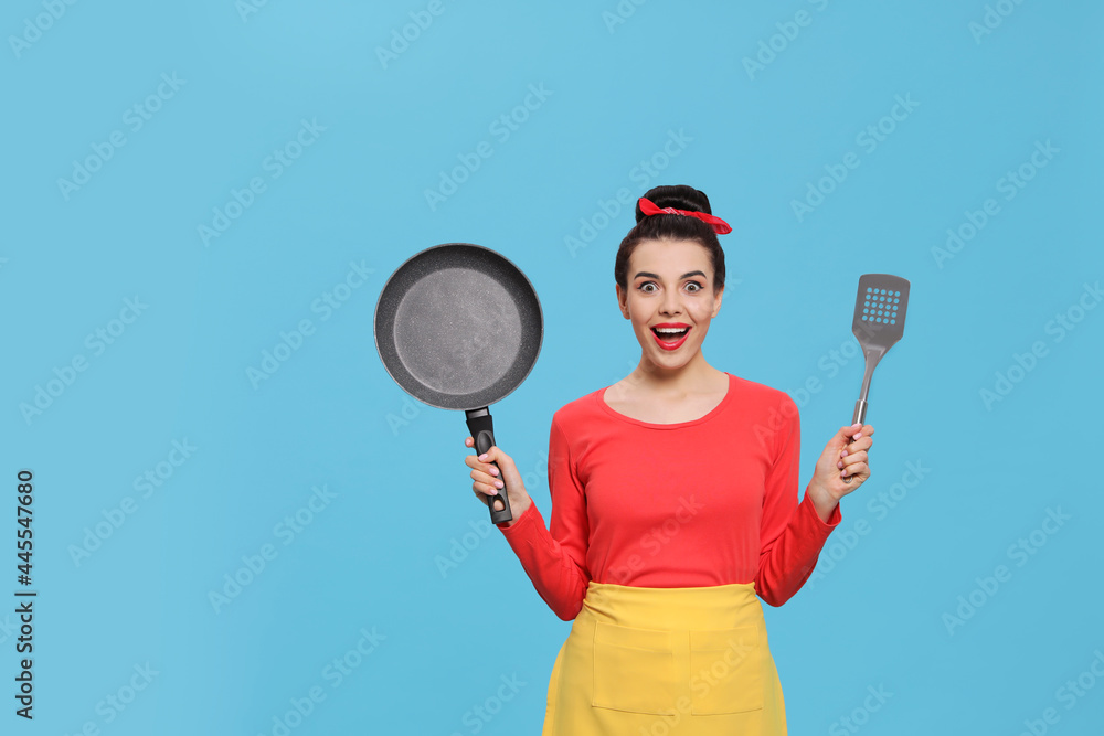 Emotional housewife with frying pan and spatula on light blue background. Space for text Emotional housewife with frying pan and spatula on light blue background. Space for text