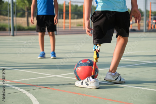 Fototapeta Naklejka Na Ścianę i Meble -  Unrecognizable children playing football, one of them has a leg prosthesis. Siblings playing sports together.