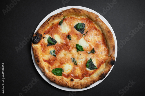 top view of margarita pizza with tomatoes, cheese and basil on black background