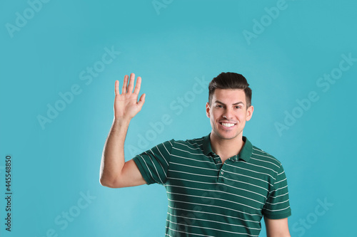 Cheerful man waving to say hello on turquoise background