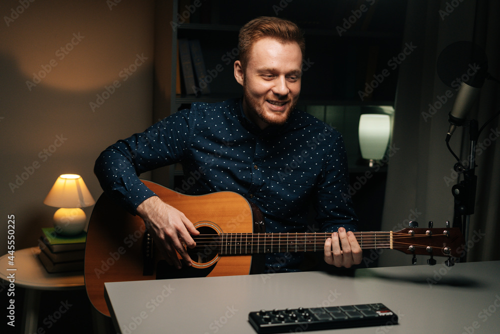 Obraz premium Portrait of guitarist singer man emotionally singing into condenser microphone and playing acoustic guitar in dark home recording studio. Creative musician leisure in apartment with modern interior.