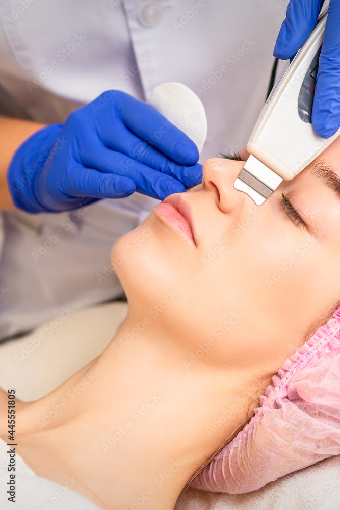 Naklejka premium Closeup of beautiful young woman receiving ultrasound facial exfoliation and cavitation facial peeling with ultrasonic equipment in cosmetology office