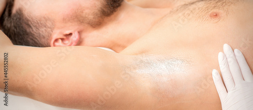 Young caucasian man receiving hair removal from his armpit in a beauty salon  depilation men s underarm