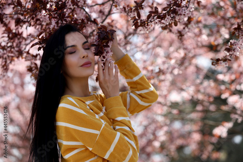 Pretty young woman near beautiful blossoming trees outdoors. Stylish spring look