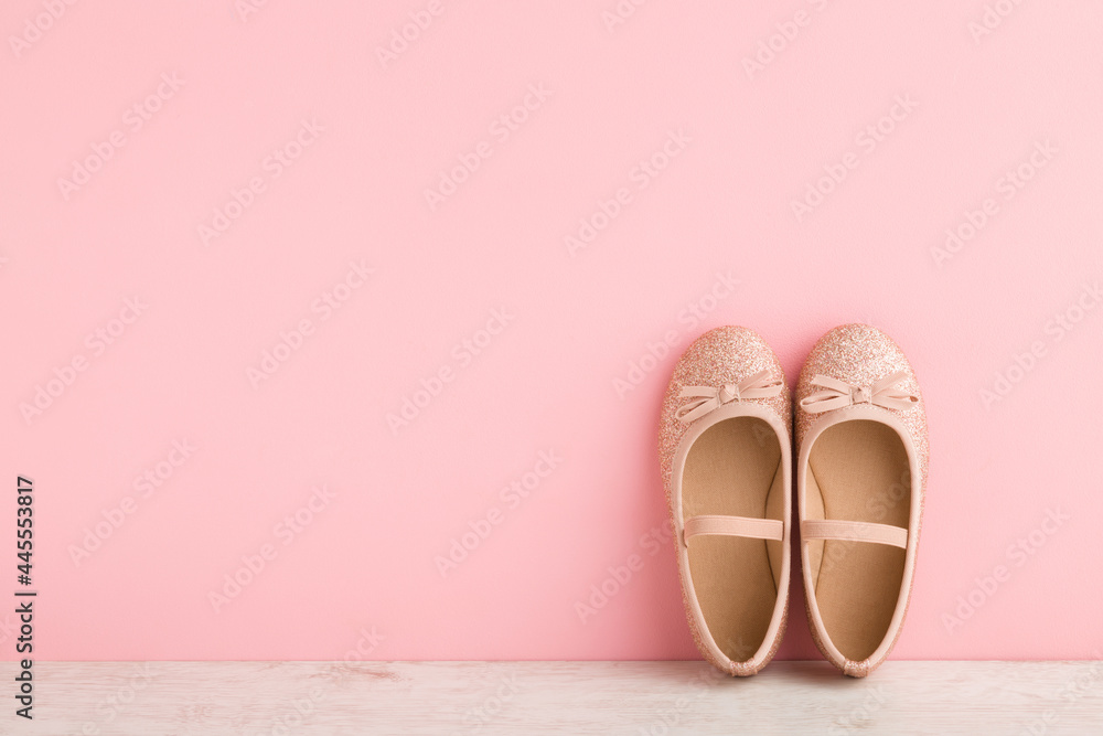 Child shiny low shoes with glitters and straps on wooden floor at light pink wall. Pastel color. Closeup. Front view. Empty place for text. - obrazy, fototapety, plakaty 