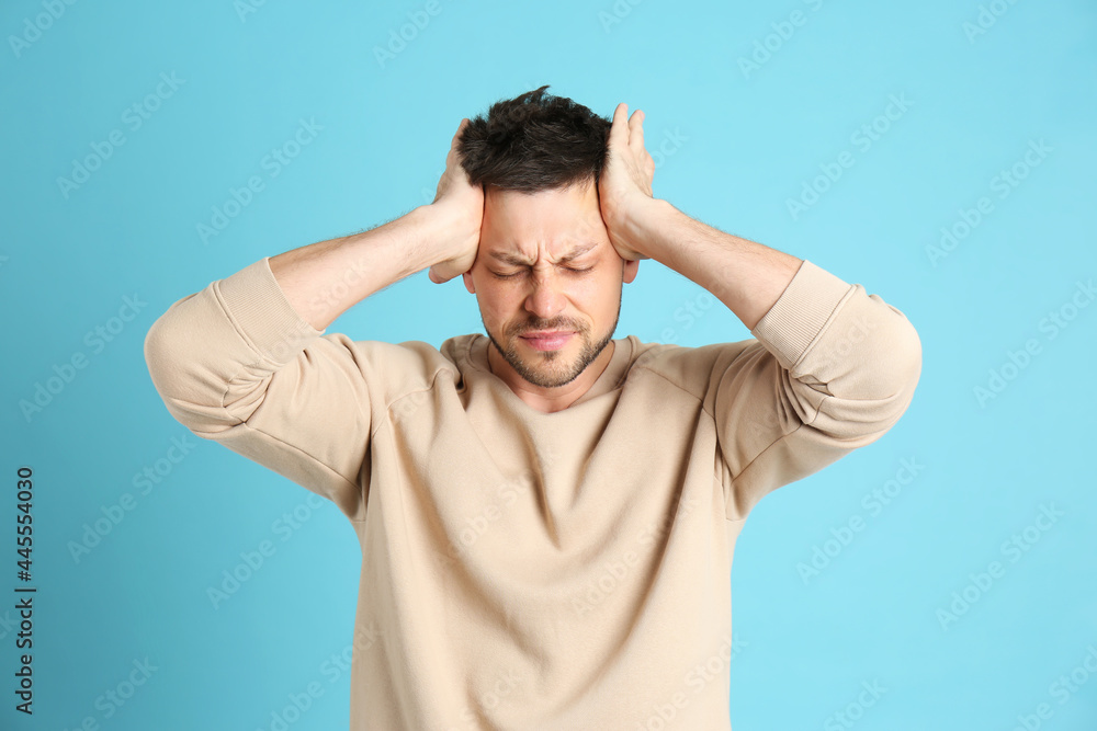 Man suffering from terrible migraine on light blue background Man suffering from terrible migraine on light blue background