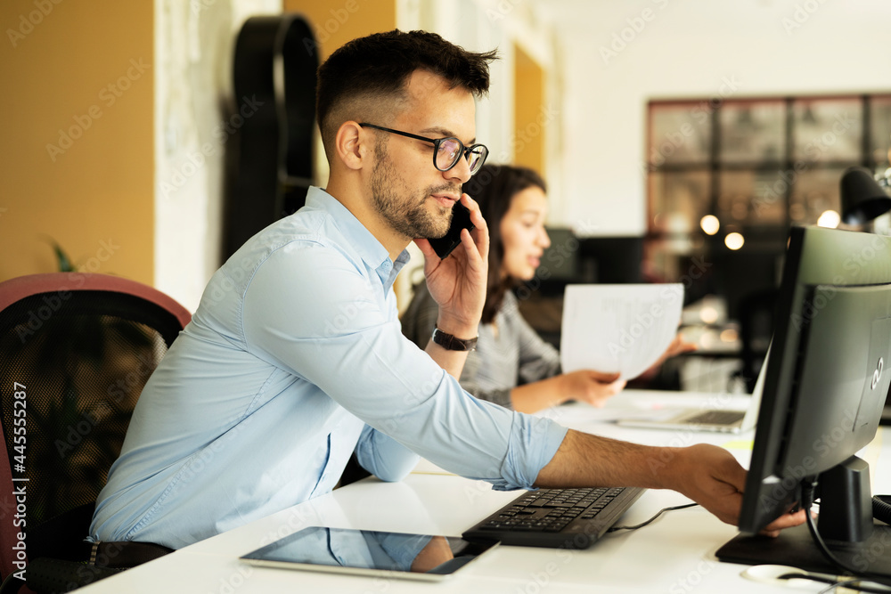 Young businessman using laptop in his office. Handsome man talking to the phone.