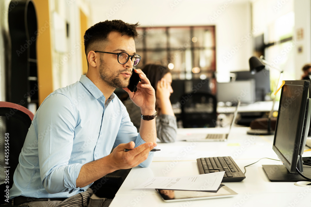 Young businessman using laptop in his office. Handsome man talking to the phone. Young businessman using laptop in his office. Handsome man talking to the phone.