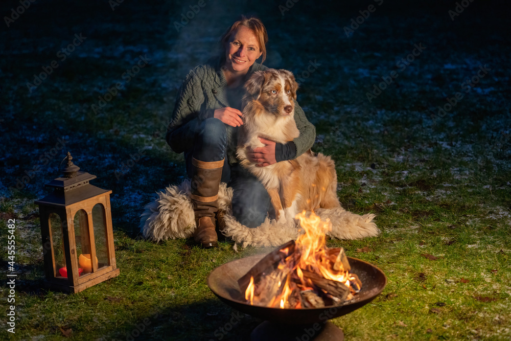 Dog sits by the campfire with his owner. The woman looks lovingly at the German Shepherd. Holiday in winter, candle fire in lantern