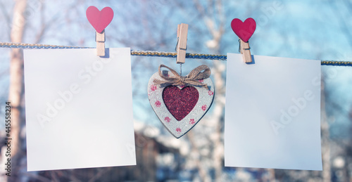 A red heart hangs on a rope between two sheets of empty paper