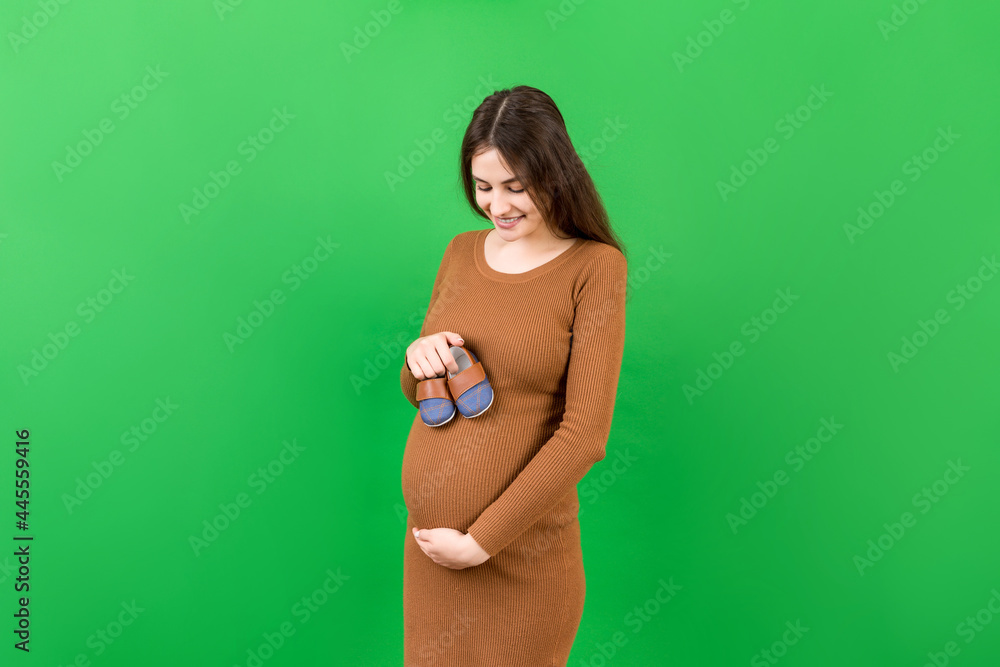 Happy pregnant woman showing small boots for a baby boy at Colored background. Future mother is waiting for a child. Copy space Happy pregnant woman showing small boots for a baby boy at Colored background. Future mother is waiting for a child. Copy space
