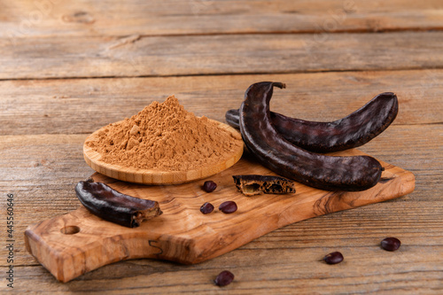 Quadro su tela Dry carob pods and carob powder over wooden background