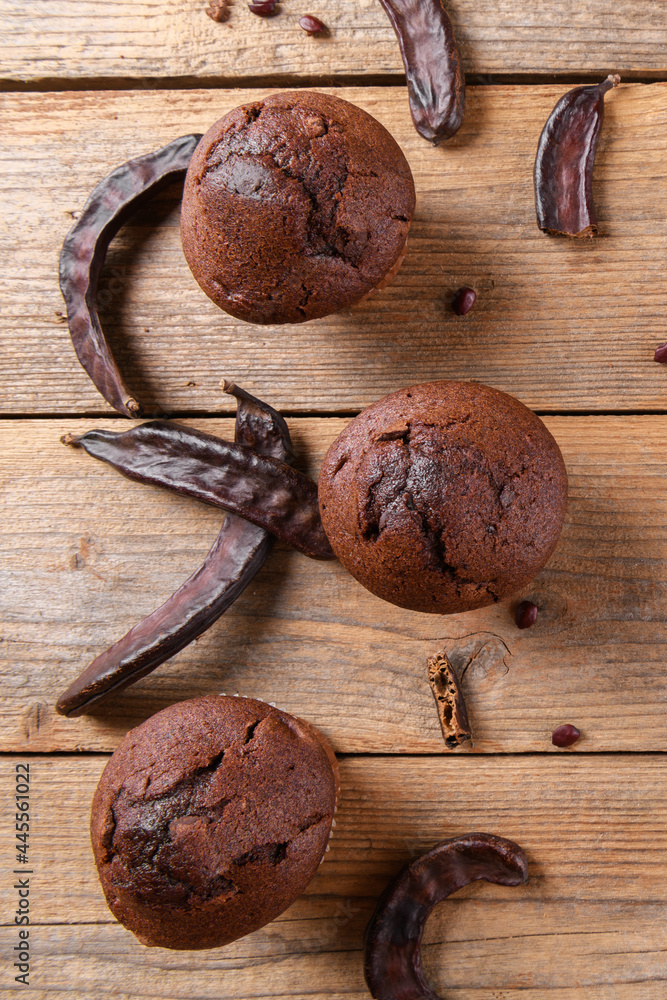Chocolate carob cupcakes cooking with carob powder and dried carob pods on a wooden background. Organic healthy sweet food for vegan vegetarian food and drinks, close up Chocolate carob cupcakes cooking with carob powder and dried carob pods on a wooden background. Organic healthy sweet food for vegan vegetarian food and drinks, close up