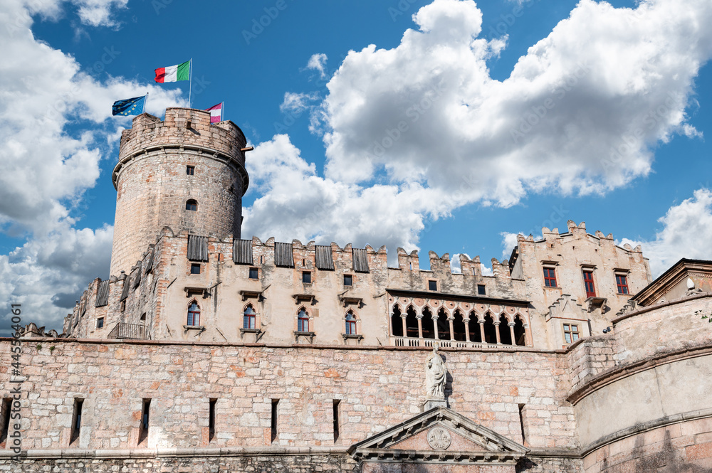 Trento, Italy, June 2021. The imposing Buonconsiglio castle, detail of the tower surmounted by the Euroopean, Italian, and regional flags. Beautiful summer day.
