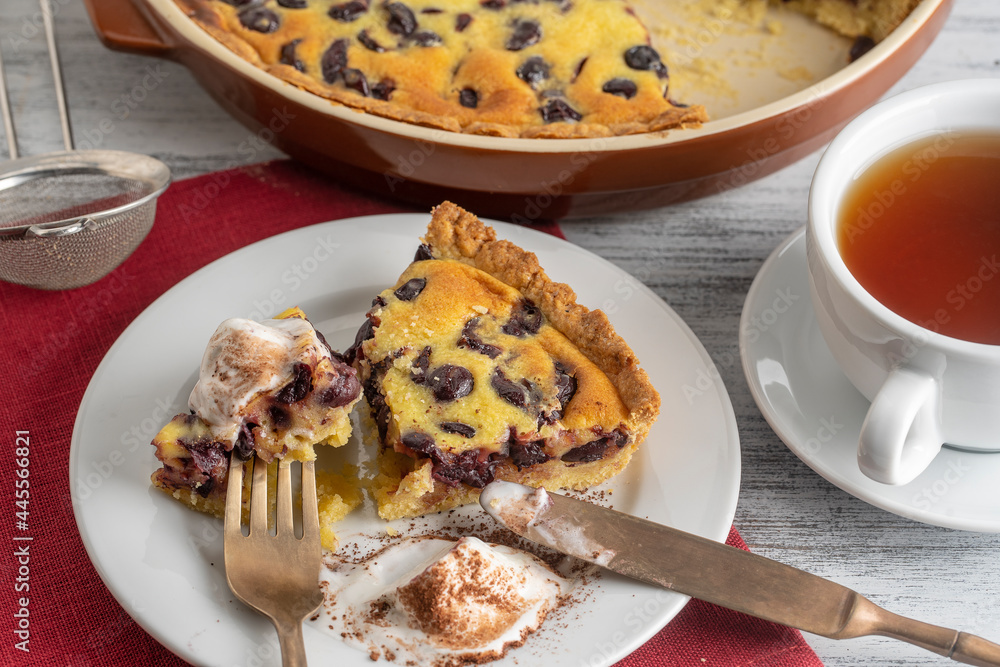 Fresh slice of cherry pie with ice cream and white cup with tea on a wooden background Fresh slice of cherry pie with ice cream and white cup with tea on a wooden background