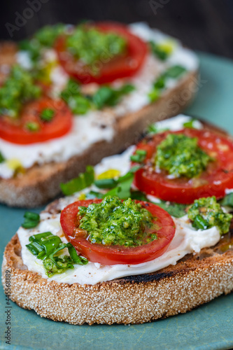 Delicious toasted bread with white cream cheese, green wild garlic and tomato on plate, close up